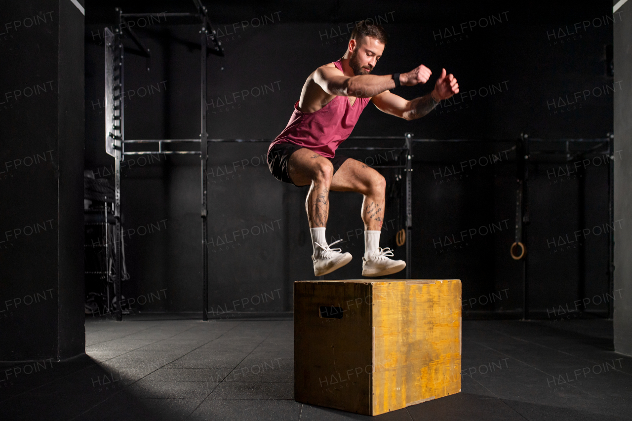 Handsome man in sportwear jumping onto yellow box. Vertical box jumps workout. Routine workout for physical and mental health.