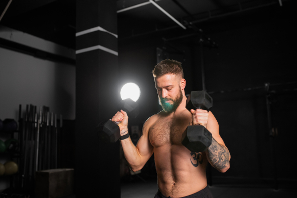 Portrait of handsome man holding dumbells in both hands. Strength exercise. Routine workout for physical and mental health.