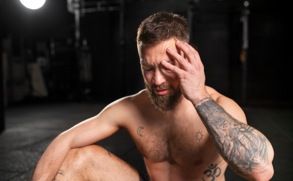 Close up of man resting after exercise, drinking water from bottle, sitting, wearing short with muscular bare chest. Routine workout for physical and mental health.