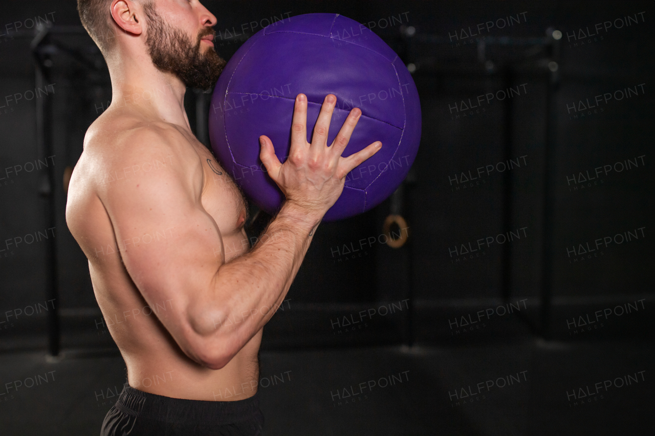 Close up of man holding dumbbell in front his muscular bare chest. Routine workout for physical and mental health.