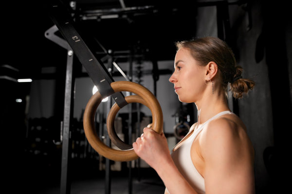 Beautiful sport woman standing by rings in gym, preparing for exercising, ring dips. Routine workout for physical and mental health.