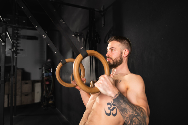 Strong man standing by rings in gym, preparing for exercising. Routine daily workout for strenght and mental health.