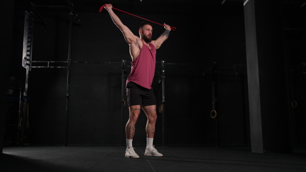 Video of handsome muscular man training with resistance band in gym, squatting. Routine workout for physical and mental health.