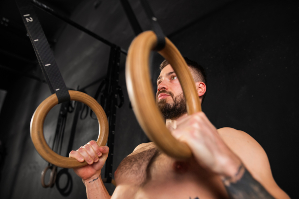 Strong man standing by rings in gym, preparing for exercising. Routine daily workout for strenght and mental health.