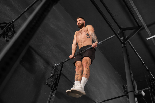 Strong man performing muscle up on bars, wearing shorts, bare chest. Crossfit workout for physical and mental health.