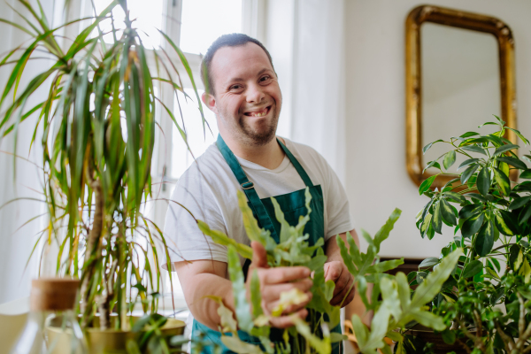 A young man with Down syndrome taking care of plants at home, smiling and looking at camera.