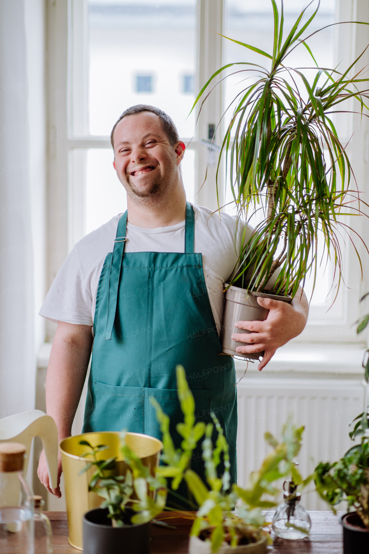 A young man with Down syndrome taking care of plants at home, smiling and looking at camera.