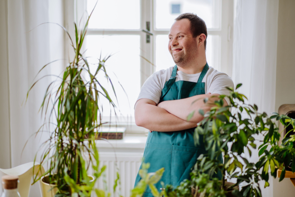 Young man with Down syndrome taking care of plants, working as sales man in fowershop.