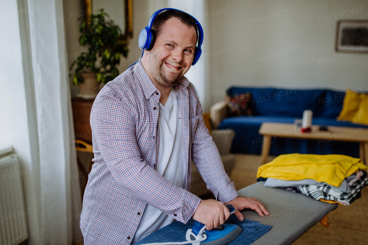 An independent young man with Down syndrome listening to music and ironing clothes at home.