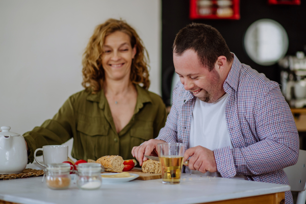 A portrait of happy man with Down syndrome with his mother at home having breakfast together.