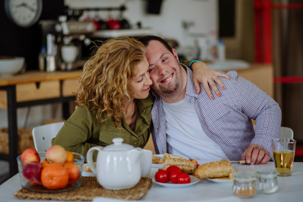 A portrait of happy man with Down syndrome with his mother at home having breakfast together.