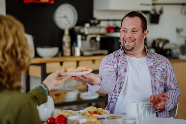 A portrait of happy man with Down syndrome with his mother at home having breakfast together.