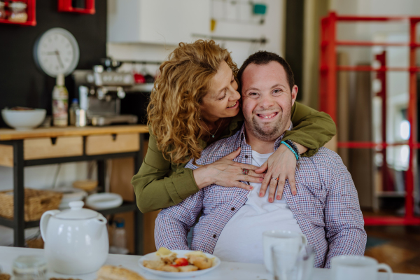 A portrait of happy man with Down syndrome with his mother at home having breakfast together.