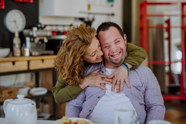 A portrait of mother hugging her grown up son with Down syndrome, motherhood concept. Looking at camera.