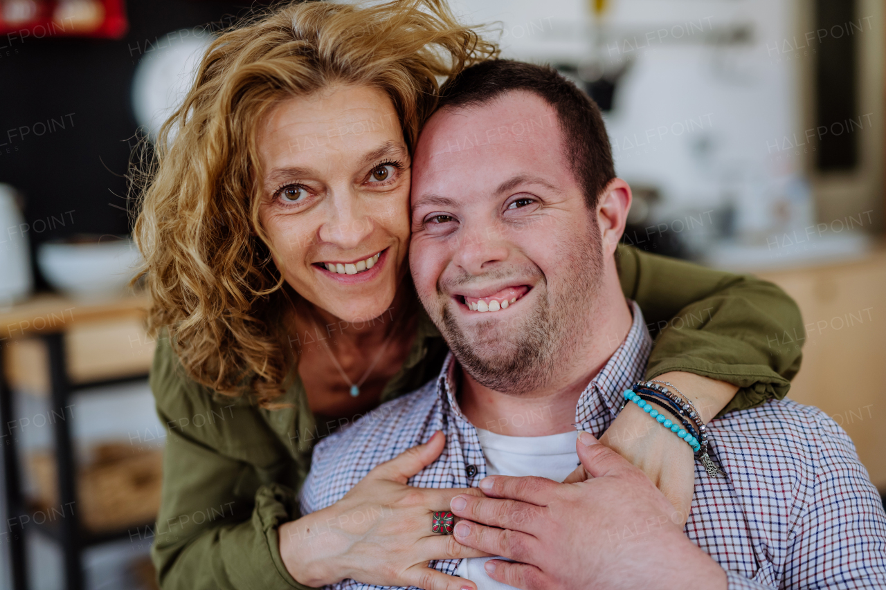 A portrait of mother hugging her grown up son with Down syndrome, motherhood concept. Looking at camera.