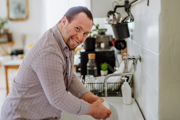 A man with down syndrome washing the dishes, taking care of himself, concept of independent and social inclusion.