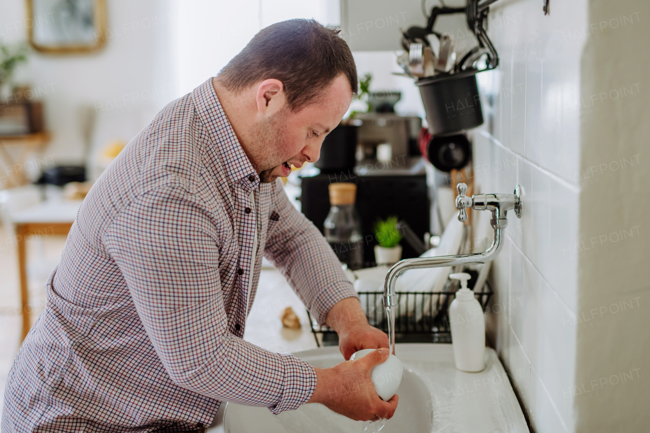 A man with down syndrome washing the dishes, taking care of himself, concept of independent and social inclusion.