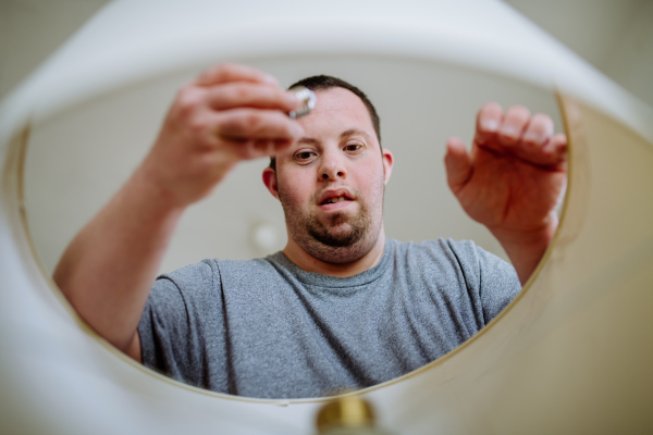 A happy young man with Down syndrome changing light bulb indoors at home