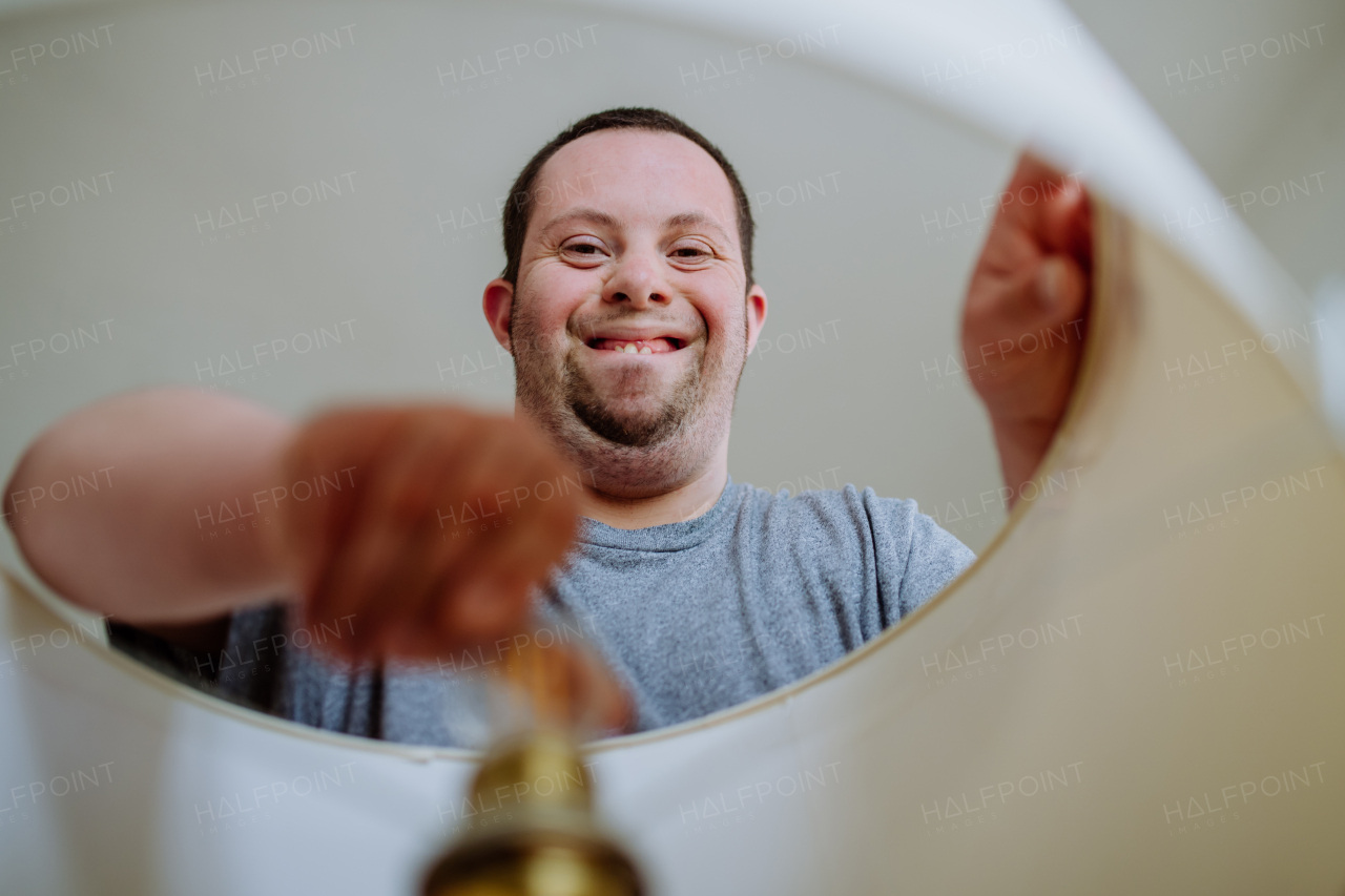 A happy young man with Down syndrome changing light bulb indoors at home