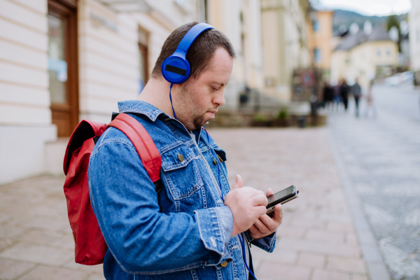 A happy young man with Down sydrome listening to music when walking in street.