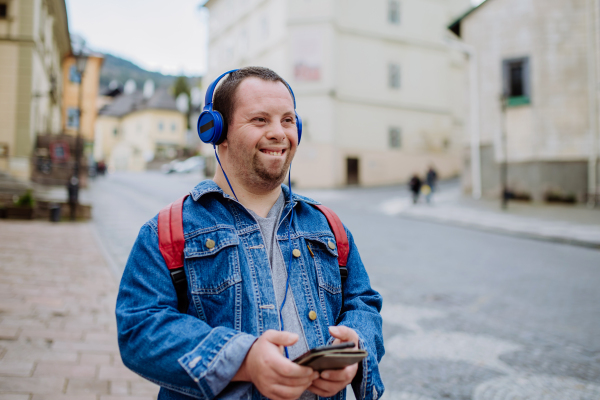 A happy young man with Down sydrome listening to music when walking in street.