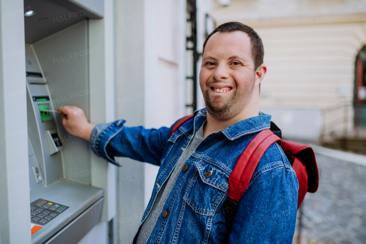 A happy young man with Down sydrome using a street ATM machine and withdrawing money.