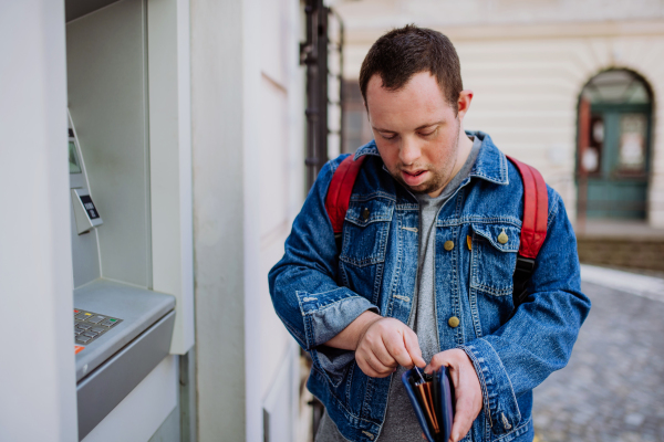 A happy young man with Down sydrome using a street ATM machine and withdrawing money.