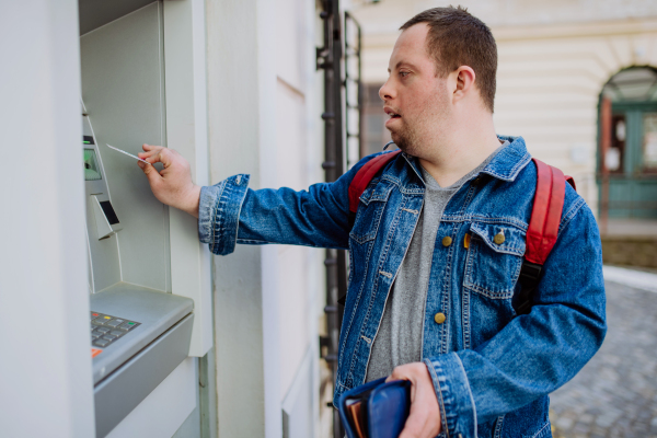 A happy young man with Down sydrome using a street ATM machine and withdrawing money.