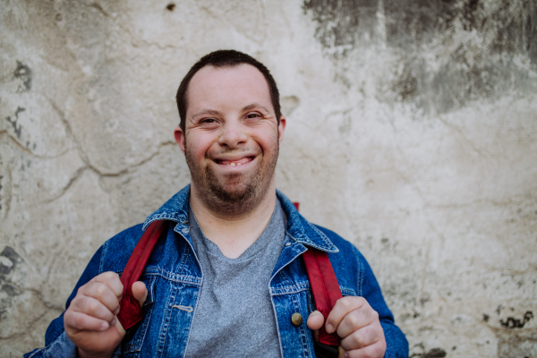 Portrait of a happy young man with Down sydrome with backpack in street, smiling.