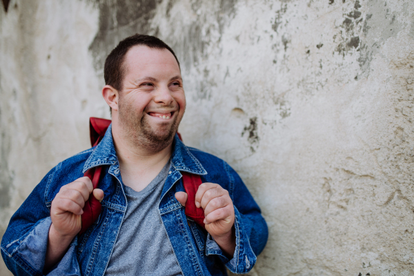 Portrait of a happy young man with Down sydrome with backpack in street, smiling.