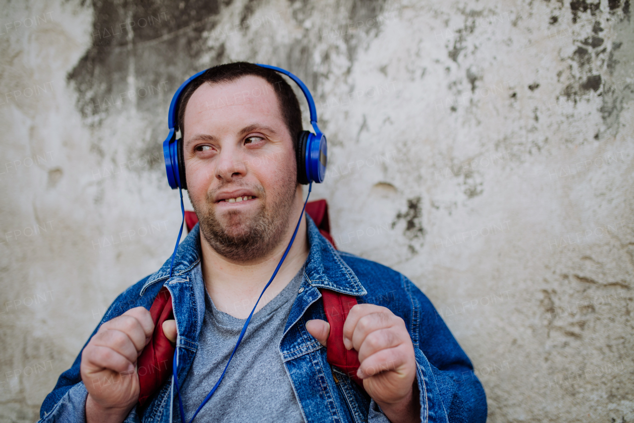 A close-up portrait of happy young man with Down sydrome listening to music when walking in street.