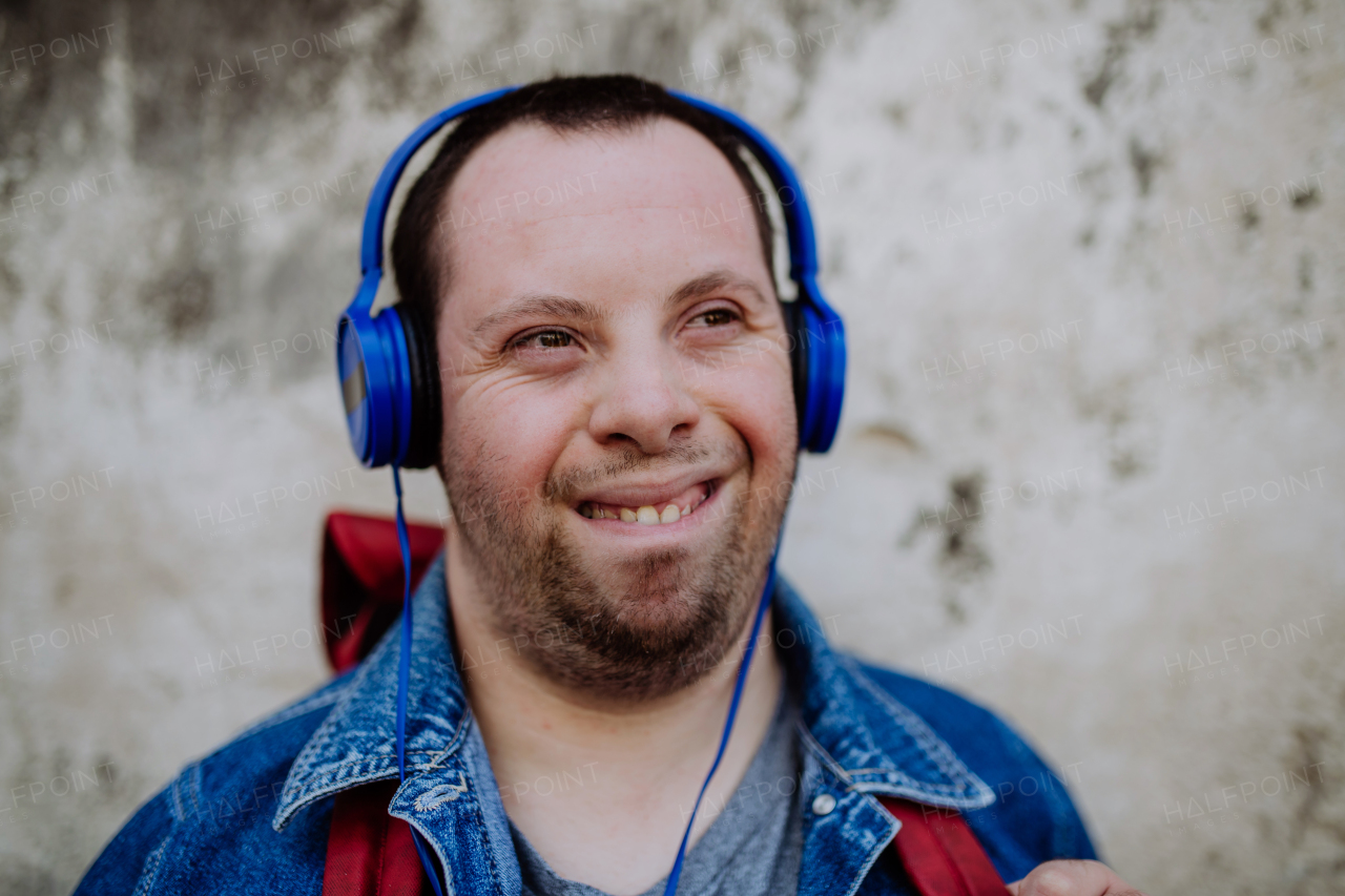 A close-up portrait of happy young man with Down sydrome listening to music when walking in street.