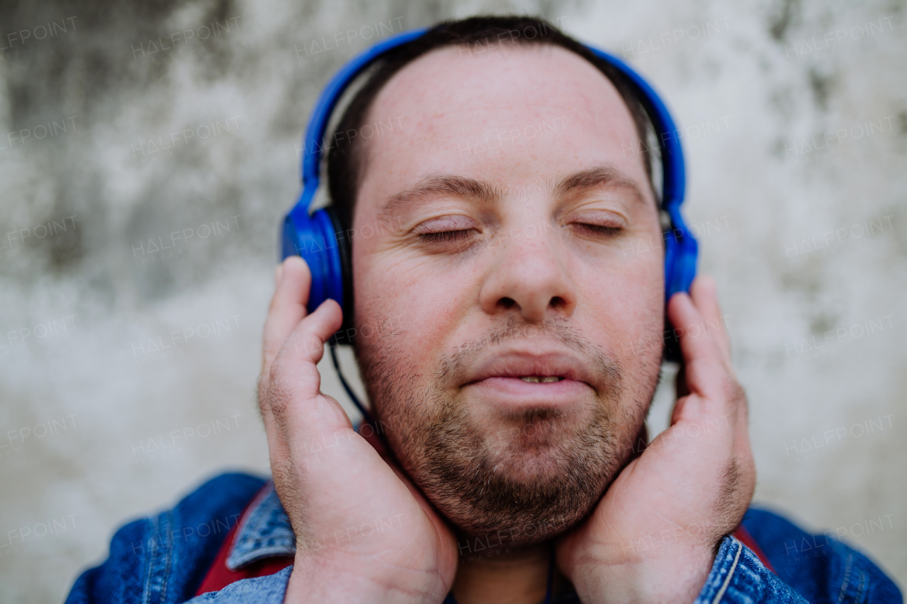 A close-up portrait of happy young man with Down sydrome listening to music when walking in street.