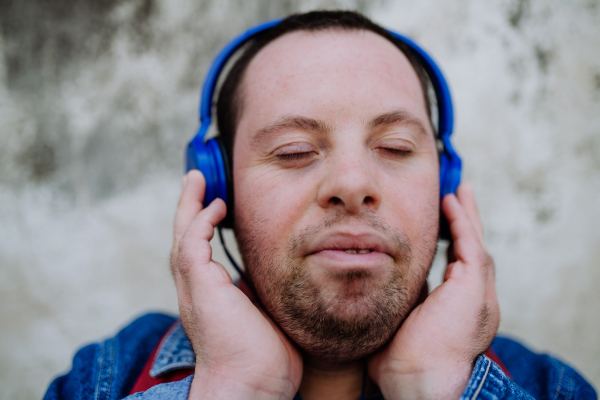 A close-up portrait of happy young man with Down sydrome listening to music when walking in street.