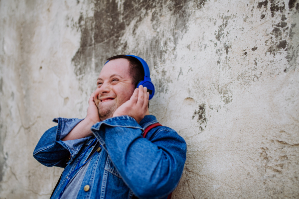 A close-up portrait of happy young man with Down sydrome listening to music when walking in street.