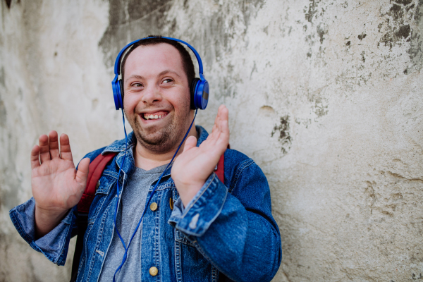 A close-up portrait of happy young man with Down sydrome listening to music when walking in street.