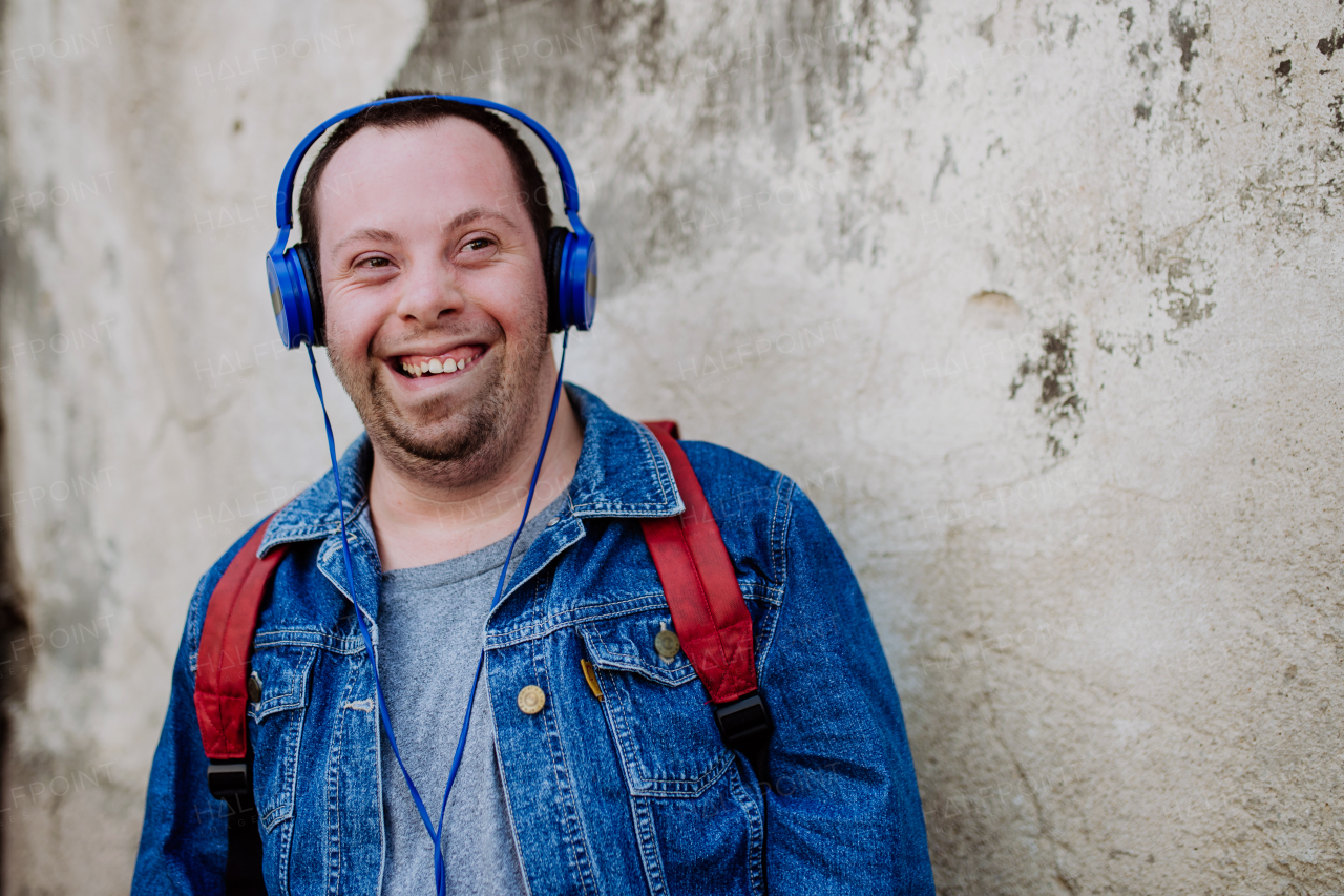 A close-up portrait of happy young man with Down sydrome listening to music when walking in street.