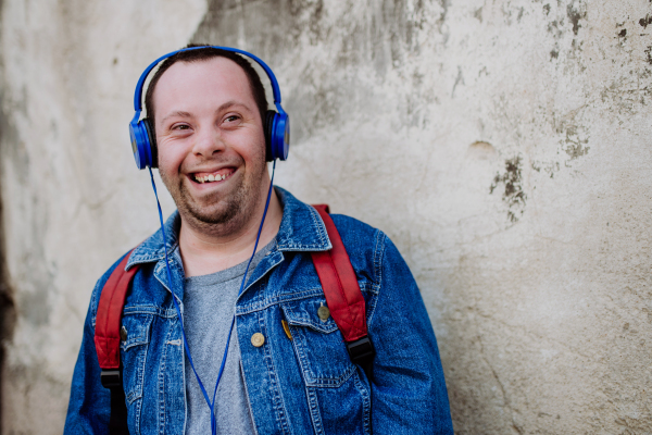 A close-up portrait of happy young man with Down sydrome listening to music when walking in street.