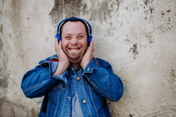 A close-up portrait of happy young man with Down sydrome listening to music when walking in street.