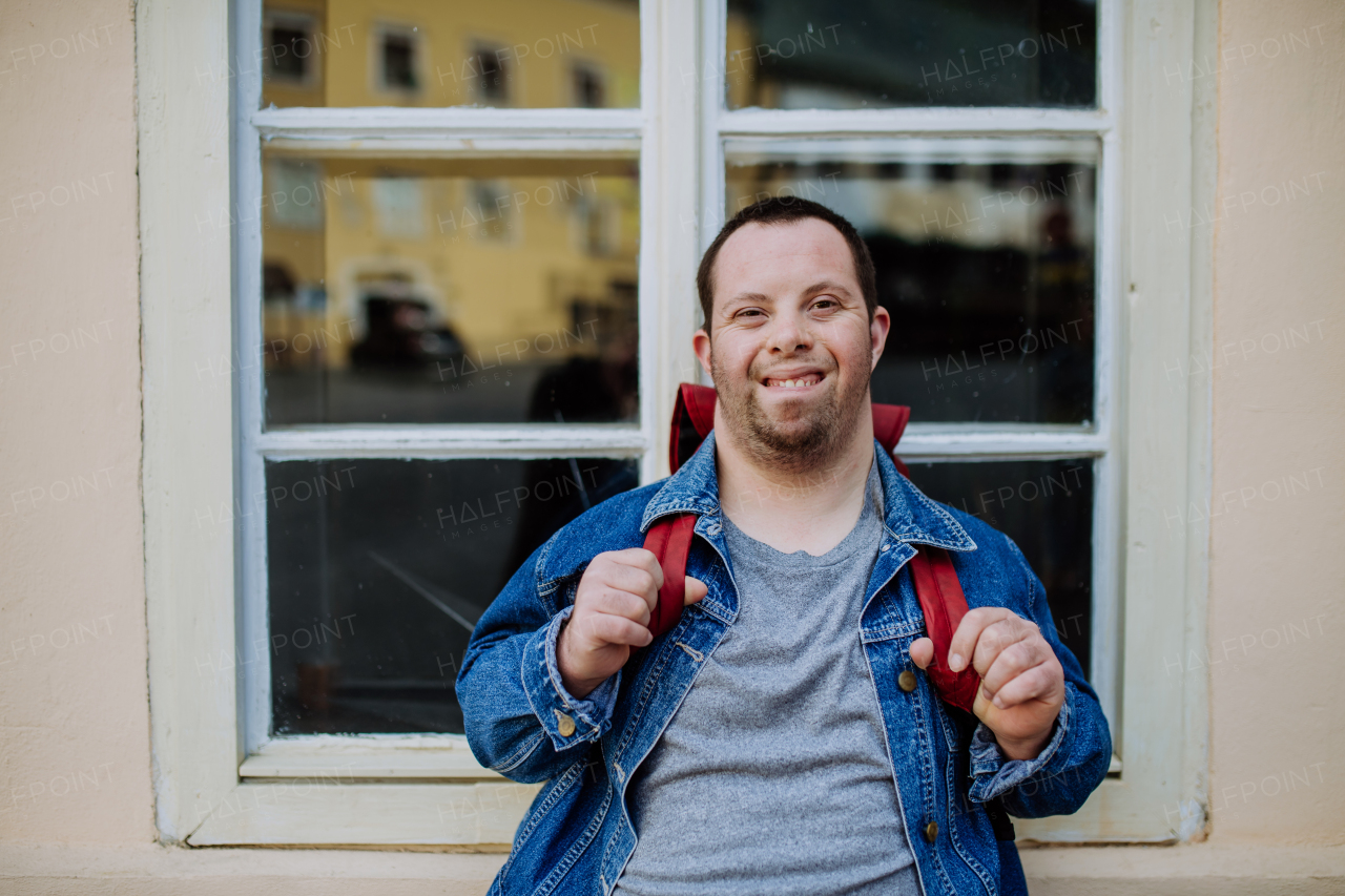 A close-up portrait of happy young man with Down sydrome with backpack in street, smiling.