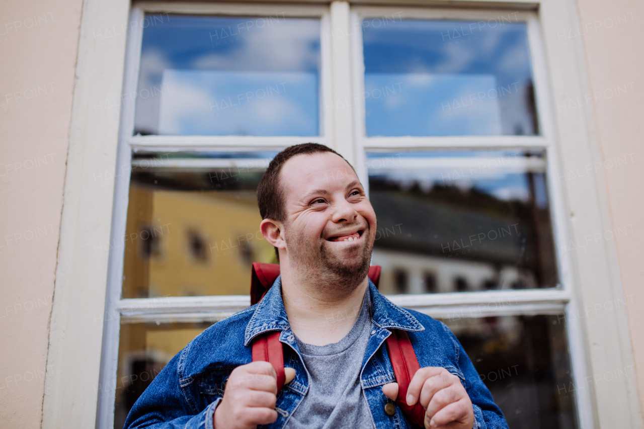 Portrait of happy young man with Down sydrome with backpack in street, smiling.