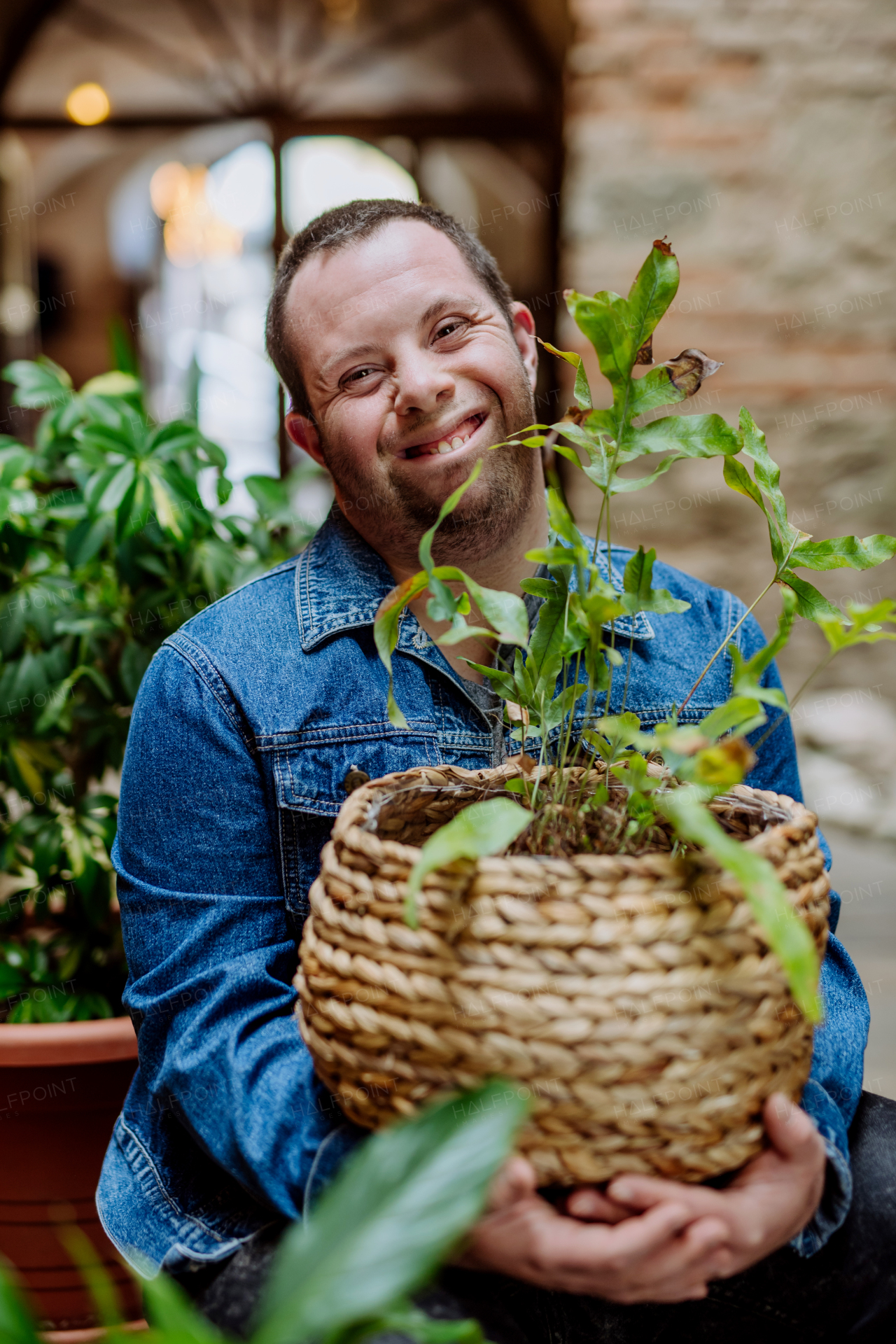 A young man with Down syndrome taking care of plants at home, smiling and looking at camera.