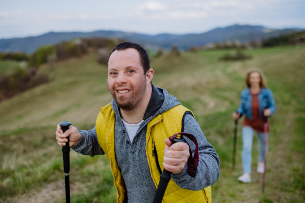 A portrait of happy young man with Down syndrome with his mother hiking together in nature.