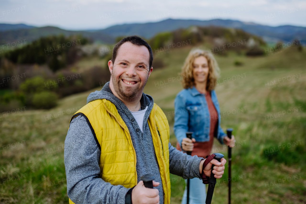 A portrait of happy young man with Down syndrome with his mother hiking together in nature.