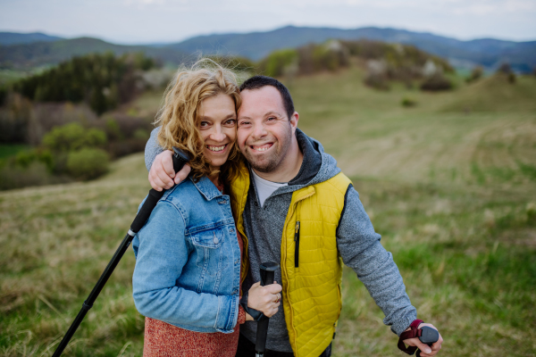 A portrait of happy young man with Down syndrome with his mother hiking together in nature.