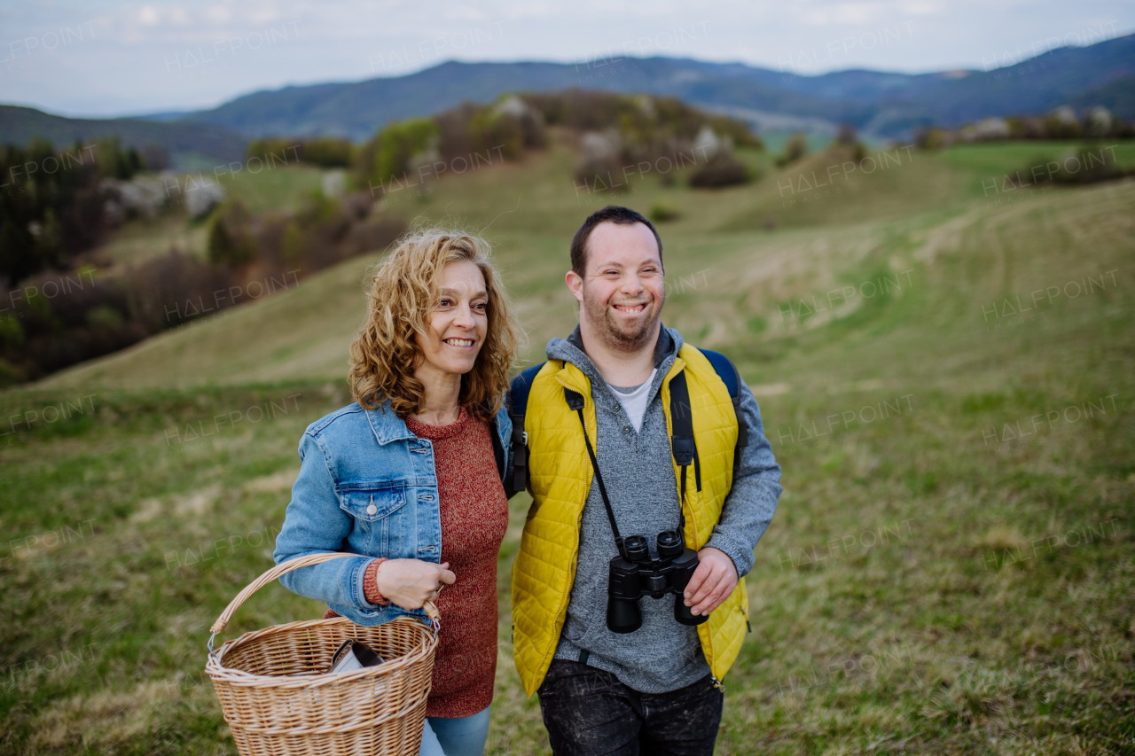 A portrait of happy young man with Down syndrome with his mother hiking together in nature.