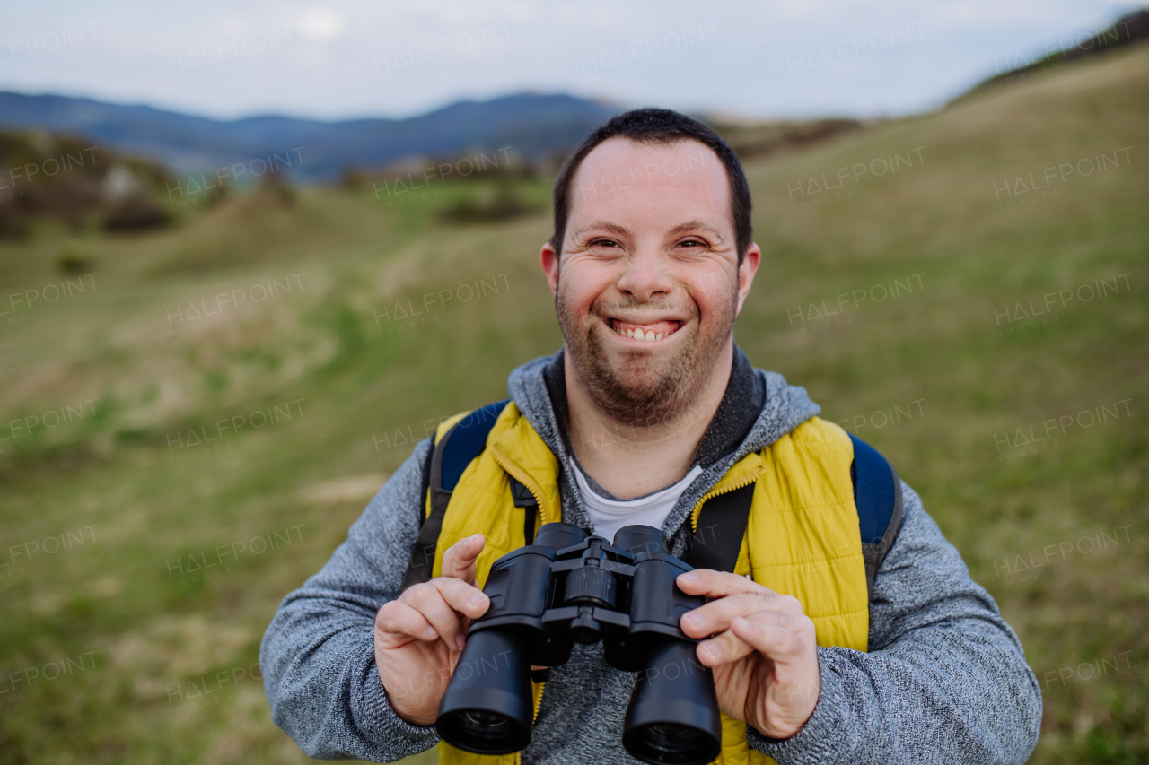 Portrait of happy young man with Down syndrome outdoor, enjoying nature and looking trough a binoculars.