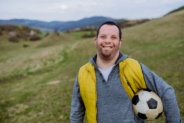 Happy young man with Down syndrome playing with a soccer ball in nature.