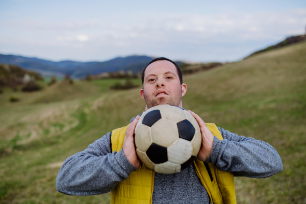 Happy young man with Down syndrome playing with a soccer ball in nature.