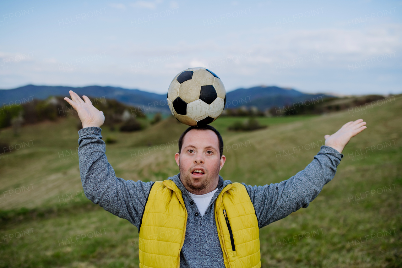 Happy young man with Down syndrome playing with a soccer ball in nature.